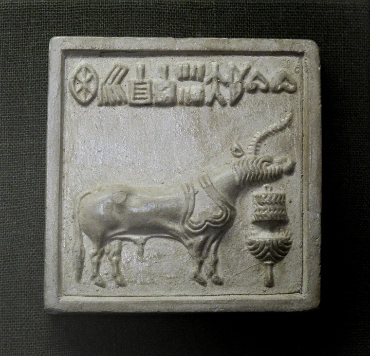 Cast of an Indus seal showing a one-horned bovine animal facing a small standing object, with a row of script signs above