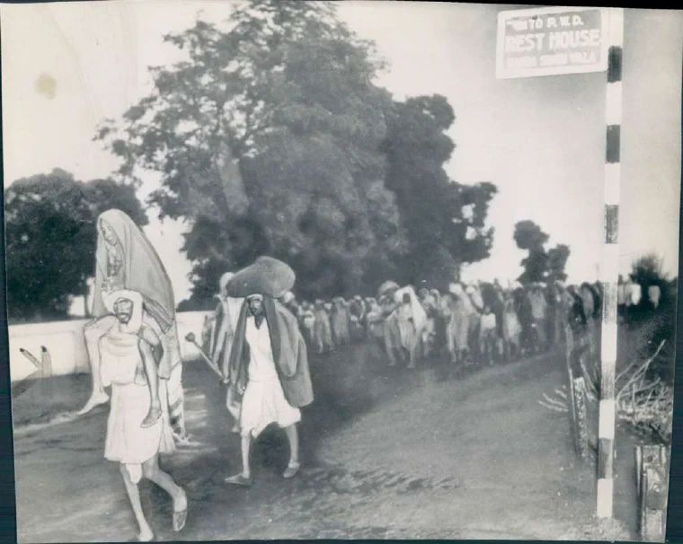 Black-and-white photograph of a crowd of refugees with bundles and carts moving along a road during the 1947 Partition