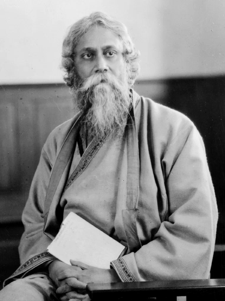 Black-and-white portrait of Rabindranath Tagore seated, holding a book, and looking toward the camera