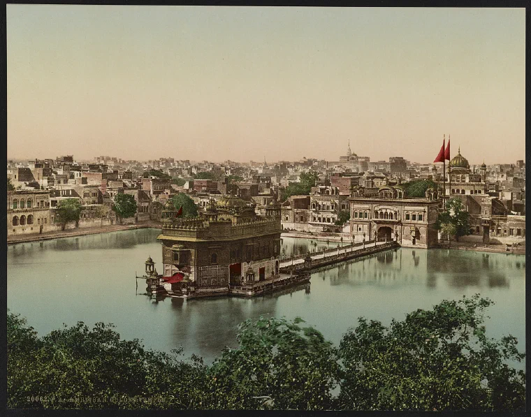 Color view from around 1900 of the Golden Temple standing in the sacred pool at Amritsar, with surrounding buildings and the city beyond